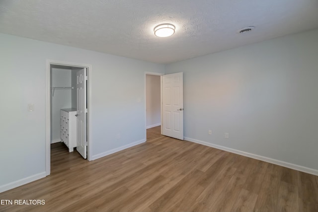 unfurnished bedroom featuring wood-type flooring, a spacious closet, a textured ceiling, and a closet