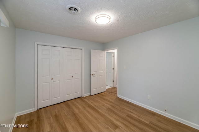 unfurnished bedroom with a textured ceiling, a closet, and light wood-type flooring