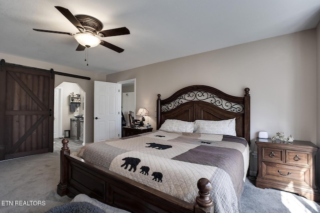 bedroom featuring connected bathroom, carpet floors, a barn door, and ceiling fan