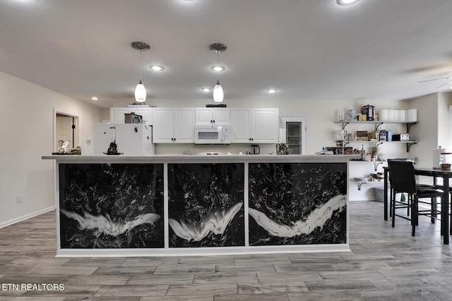 kitchen featuring hanging light fixtures, a center island, white cabinets, and white appliances