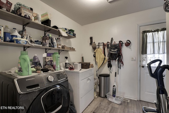 laundry area with a textured ceiling, independent washer and dryer, and light hardwood / wood-style flooring