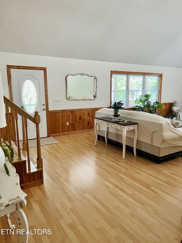 living area with stairway, light wood-type flooring, wainscoting, and a textured ceiling