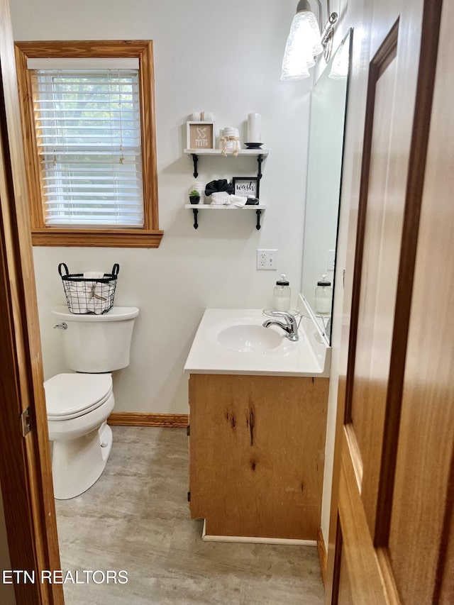 half bath featuring baseboards, vanity, and toilet