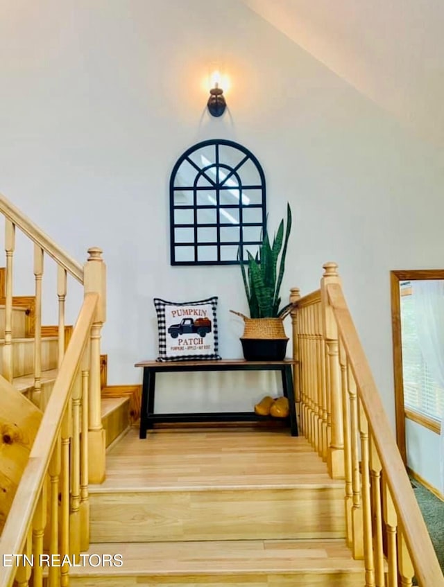 staircase with a high ceiling, wainscoting, and wood finished floors