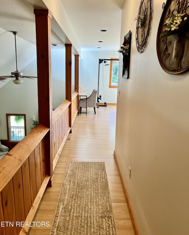 hallway with light wood finished floors, decorative columns, and baseboards