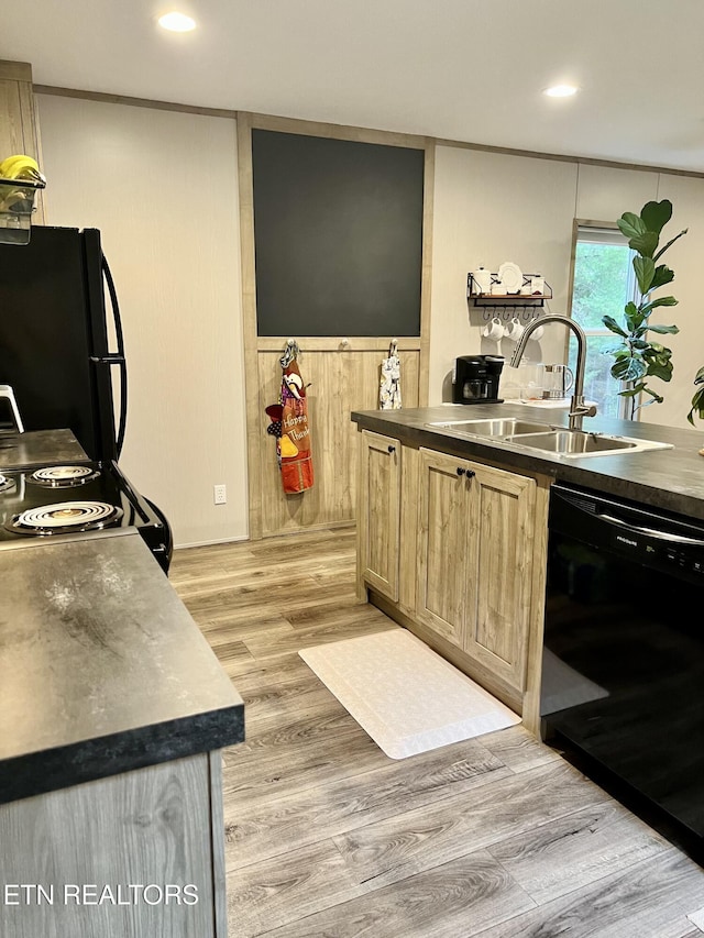 kitchen with a sink, light wood-style floors, wainscoting, black appliances, and dark countertops