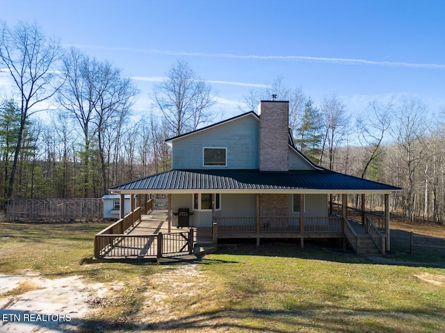 view of front of house with covered porch, a chimney, metal roof, and a front yard