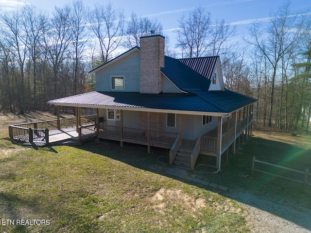 rear view of house with a deck, a chimney, metal roof, and a yard