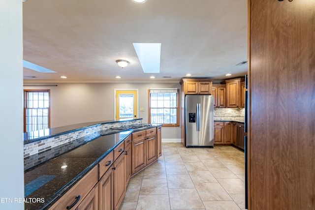 kitchen with light tile patterned flooring, tasteful backsplash, a skylight, dark stone countertops, and stainless steel fridge