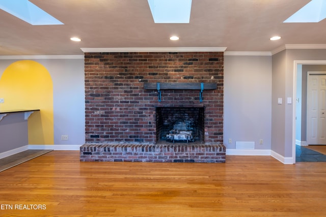 unfurnished living room featuring a skylight, a fireplace, ornamental molding, and light hardwood / wood-style floors