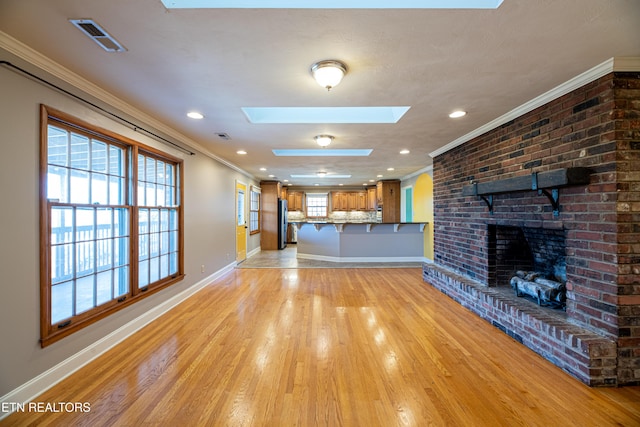 unfurnished living room with ornamental molding, light hardwood / wood-style floors, a fireplace, and a skylight