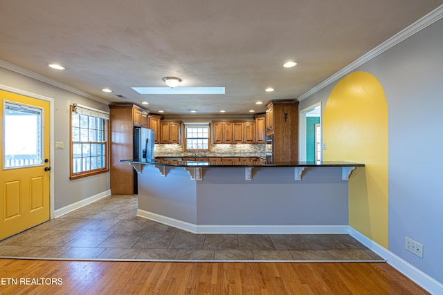 kitchen featuring stainless steel fridge, a breakfast bar, wood-type flooring, ornamental molding, and kitchen peninsula