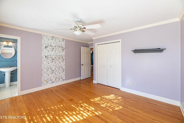 unfurnished bedroom featuring ensuite bath, ornamental molding, a closet, hardwood / wood-style flooring, and ceiling fan