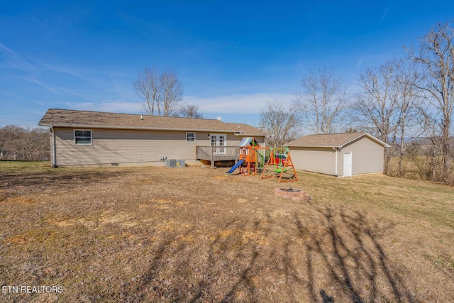 back of property featuring a lawn, an outdoor fire pit, a wooden deck, a playground, and a storage unit