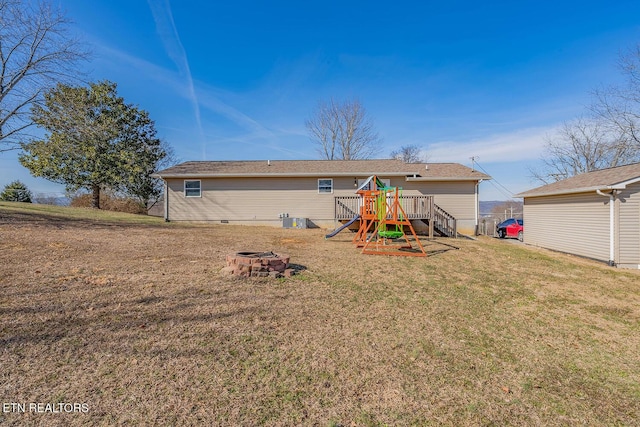 rear view of house featuring a playground, a yard, and an outdoor fire pit