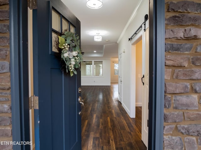 hallway with dark wood-type flooring, ornamental molding, and a barn door