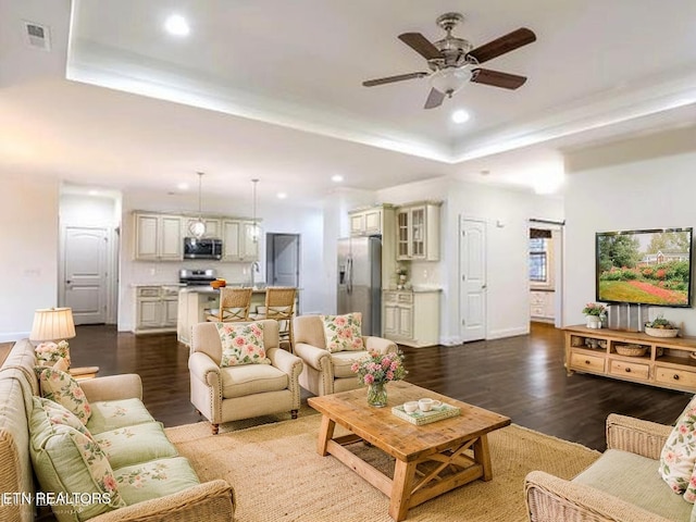 living room featuring a raised ceiling, recessed lighting, dark wood-type flooring, and baseboards