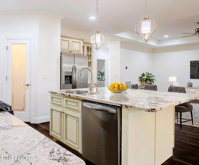 kitchen with cream cabinets, stainless steel appliances, a sink, dark wood-style flooring, and light stone countertops