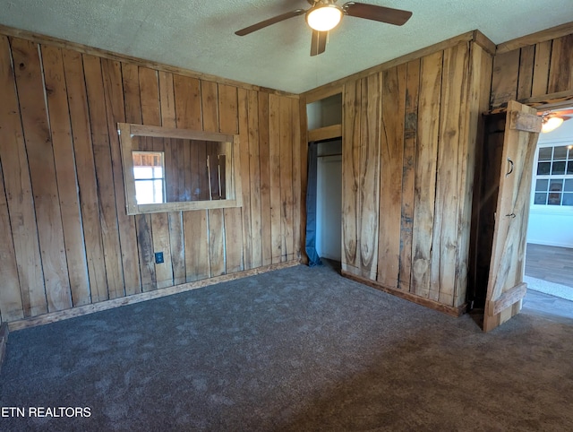 unfurnished bedroom with dark colored carpet, wooden walls, a textured ceiling, and ceiling fan