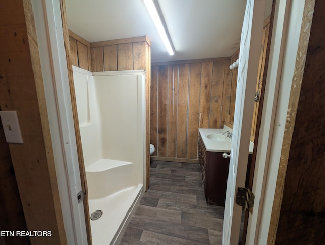 bathroom with toilet, a shower, wood walls, vanity, and hardwood / wood-style flooring