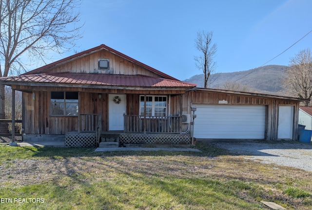 view of front of house featuring a porch, a mountain view, gravel driveway, a front yard, and a garage