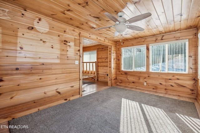 empty room featuring wooden walls, wooden ceiling, ceiling fan, and carpet flooring