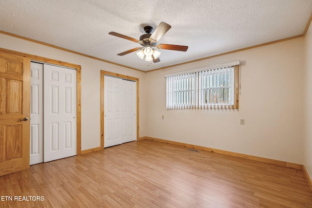 unfurnished bedroom with two closets, a textured ceiling, ceiling fan, and light hardwood / wood-style flooring