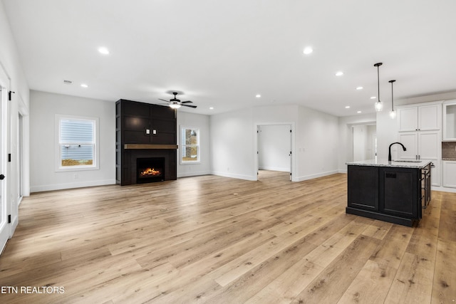 living room with sink, light hardwood / wood-style floors, a large fireplace, and ceiling fan