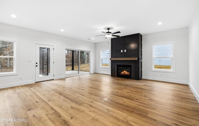 unfurnished living room with ceiling fan, plenty of natural light, a fireplace, and light wood-type flooring