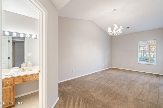 carpeted empty room featuring an inviting chandelier and vaulted ceiling