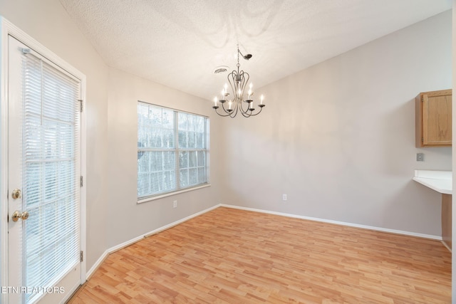 unfurnished dining area featuring lofted ceiling, a chandelier, a textured ceiling, and light hardwood / wood-style flooring