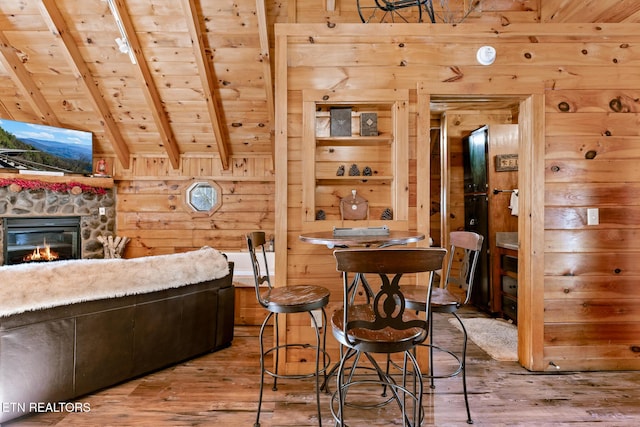 dining area featuring a stone fireplace, wood walls, vaulted ceiling with beams, hardwood / wood-style flooring, and wood ceiling