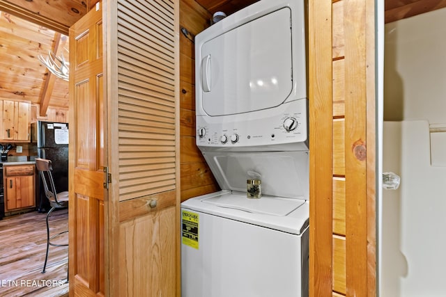 laundry area with light hardwood / wood-style floors, stacked washer and clothes dryer, and wood walls