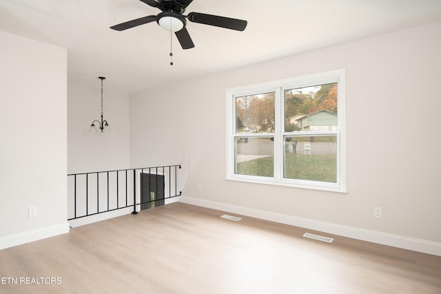 spare room featuring ceiling fan with notable chandelier, light hardwood / wood-style floors, and a wealth of natural light