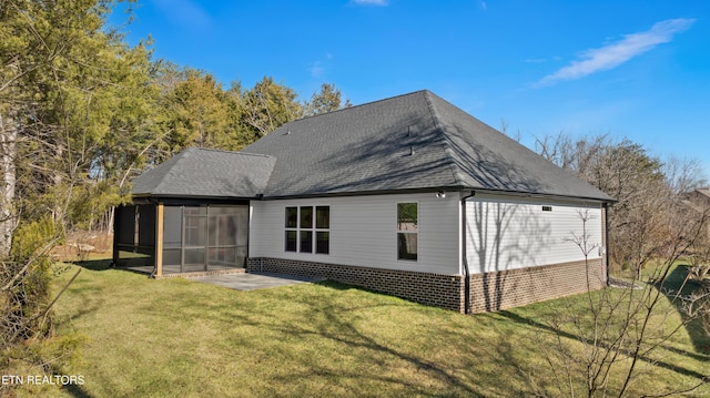 rear view of house featuring a yard, a sunroom, roof with shingles, and a patio