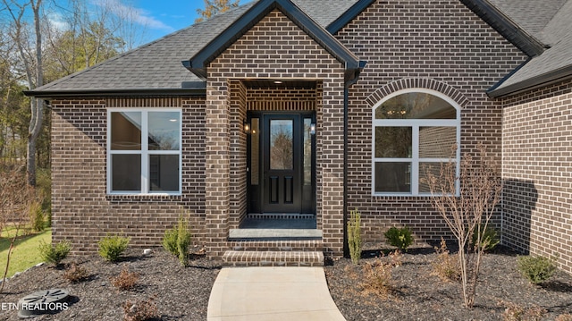 doorway to property with a shingled roof and brick siding