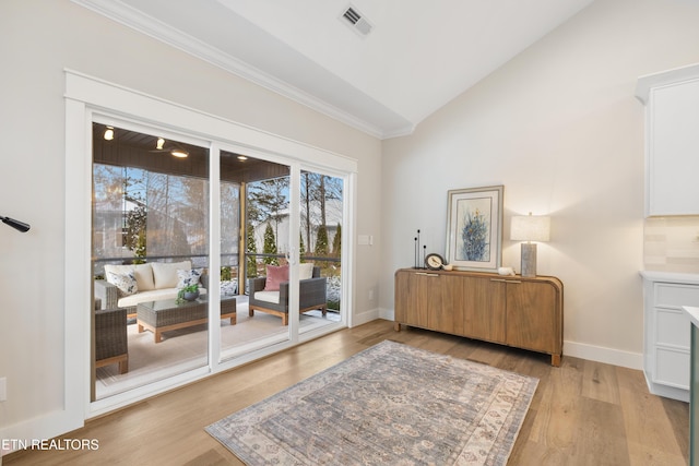 entryway with baseboards, visible vents, ornamental molding, vaulted ceiling, and light wood-style floors