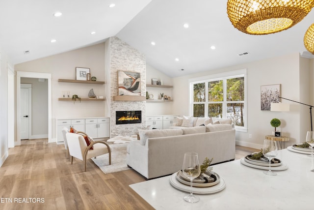 living room with visible vents, a stone fireplace, light wood-type flooring, high vaulted ceiling, and recessed lighting