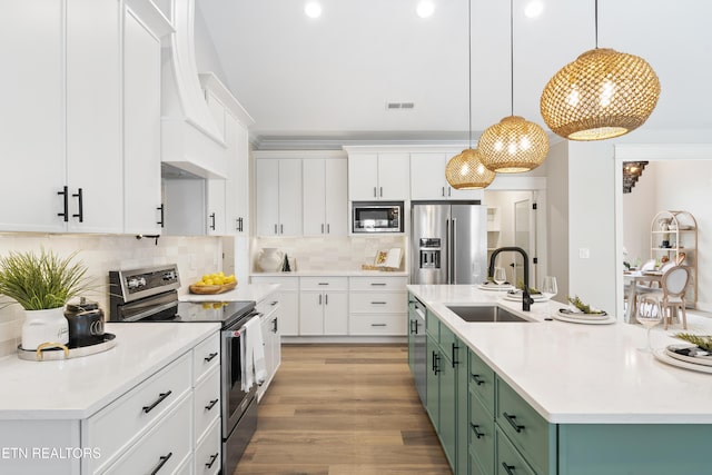 kitchen with a kitchen island with sink, a sink, light countertops, appliances with stainless steel finishes, and green cabinetry