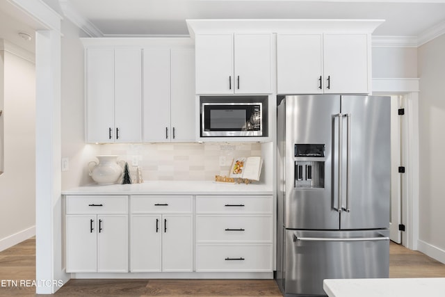 kitchen featuring white cabinets, high quality fridge, ornamental molding, built in microwave, and light countertops