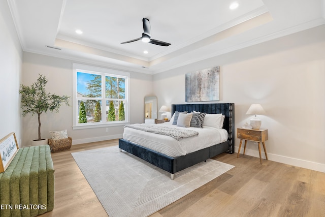 bedroom with light wood finished floors, a raised ceiling, visible vents, ornamental molding, and baseboards