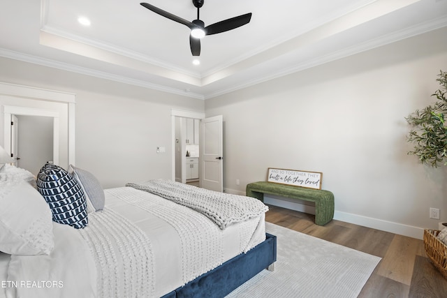 bedroom with a tray ceiling, recessed lighting, ornamental molding, wood finished floors, and baseboards