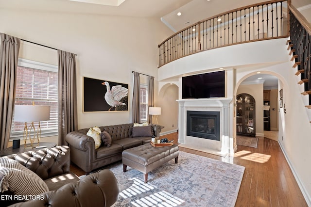 living room with baseboards, a fireplace with flush hearth, wood finished floors, and a towering ceiling