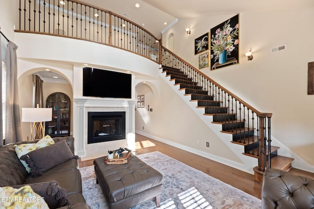 living area with visible vents, stairs, a high ceiling, wood finished floors, and a glass covered fireplace