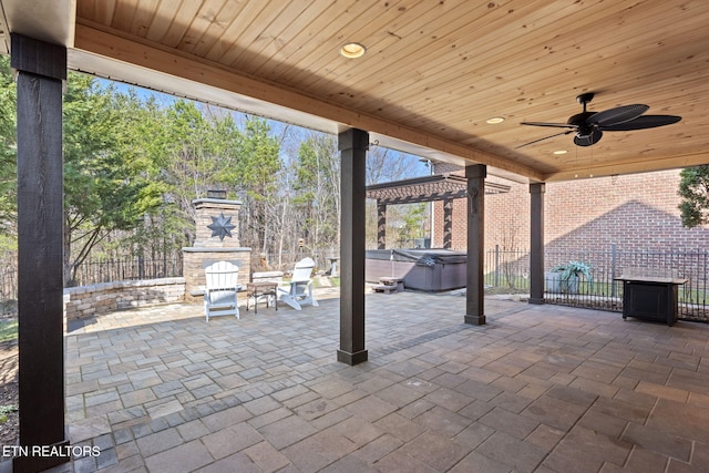 view of patio with a ceiling fan, fence, an outdoor fireplace, and a hot tub