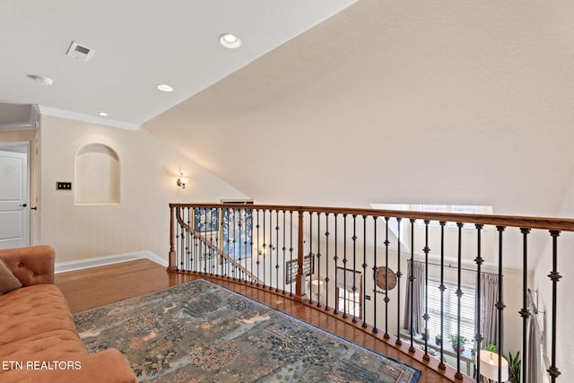 corridor with visible vents, lofted ceiling, wood finished floors, crown molding, and baseboards