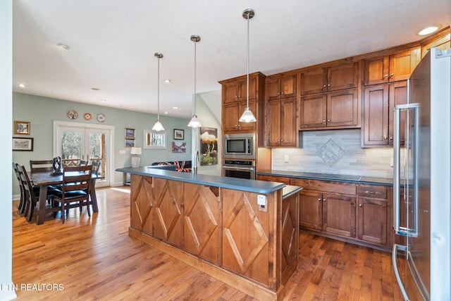 kitchen with dark wood-type flooring, hanging light fixtures, appliances with stainless steel finishes, a kitchen island, and backsplash