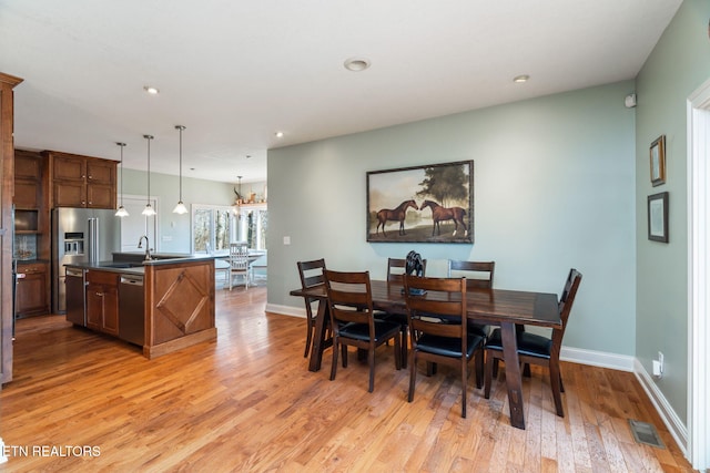 dining space featuring sink, a chandelier, and light wood-type flooring