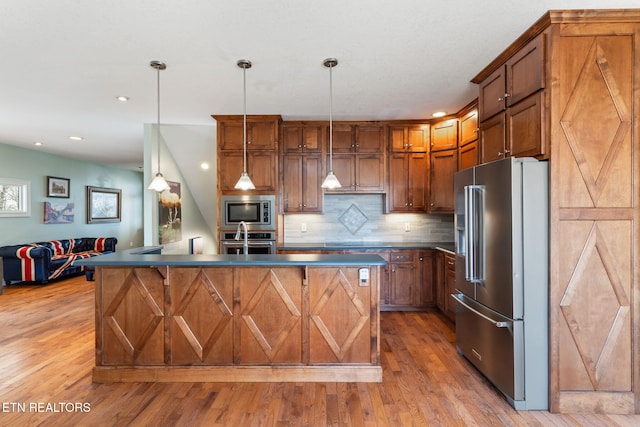 kitchen with hanging light fixtures, appliances with stainless steel finishes, light hardwood / wood-style floors, a kitchen island with sink, and backsplash