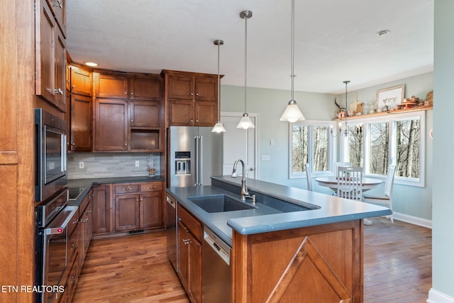 kitchen featuring an island with sink, sink, backsplash, hanging light fixtures, and stainless steel appliances